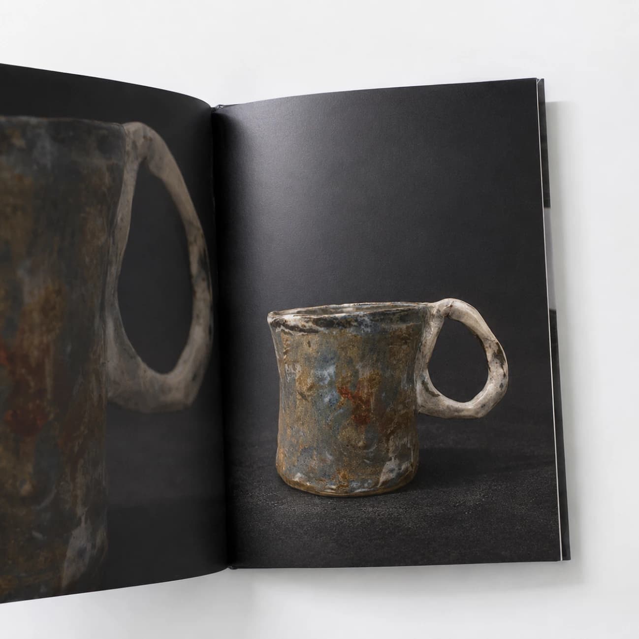 An open portfolio showing a mottled ceramic mug and a close-up of its handle.