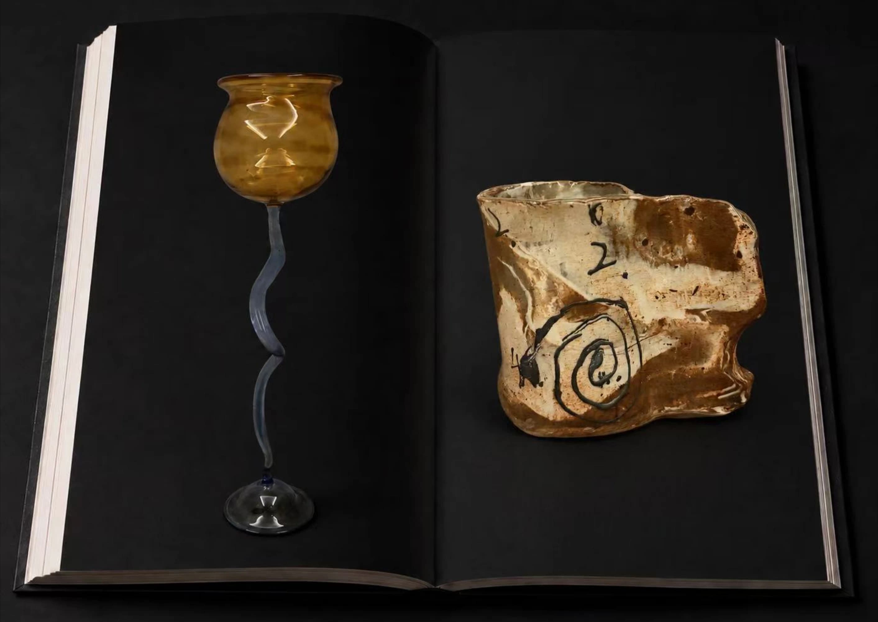 An open portfolio showing a yellow goblet with a curved stem and a patterned ceramic vessel.
