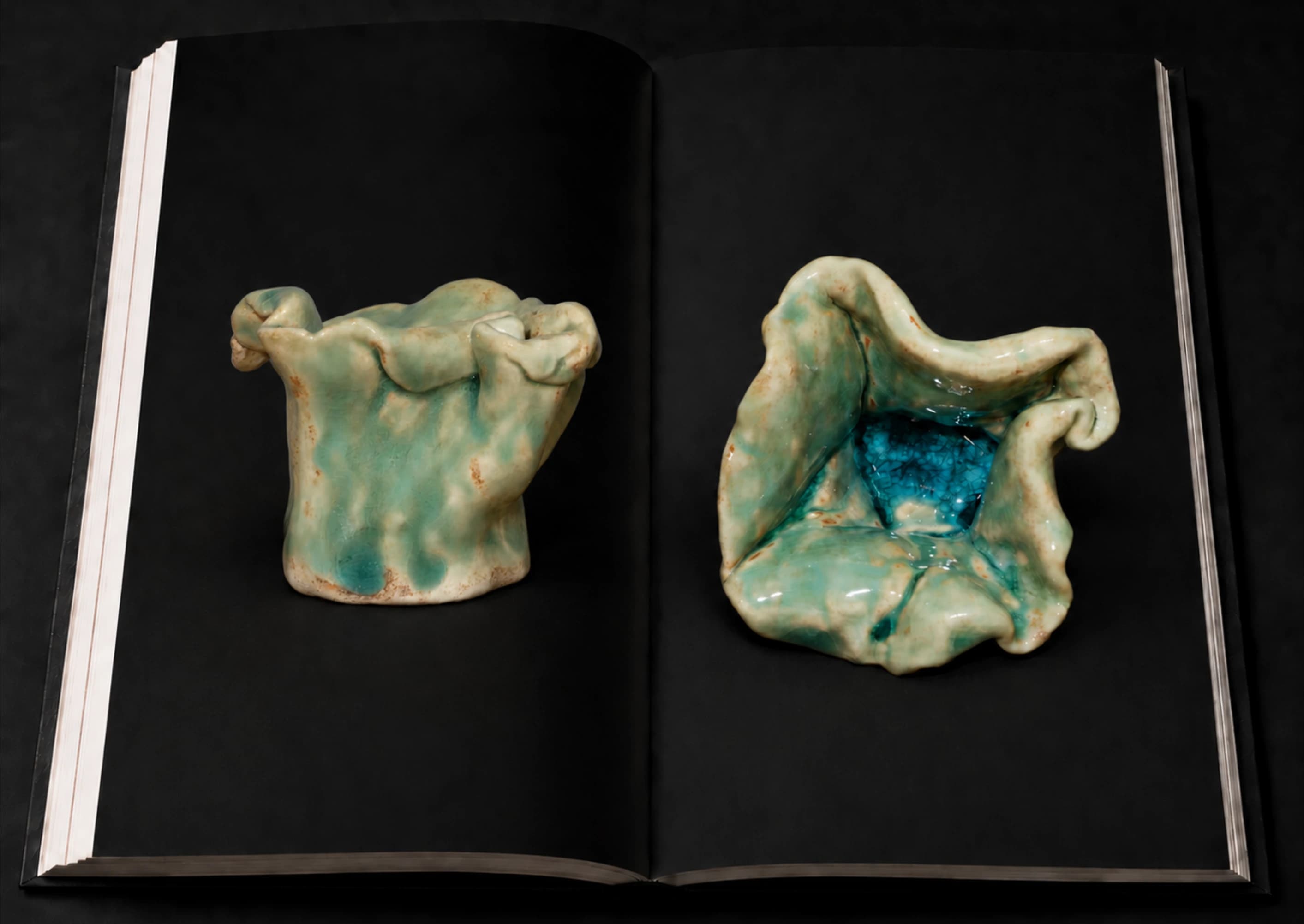 An open portfolio showing two views of a folded turquoise ceramic form.