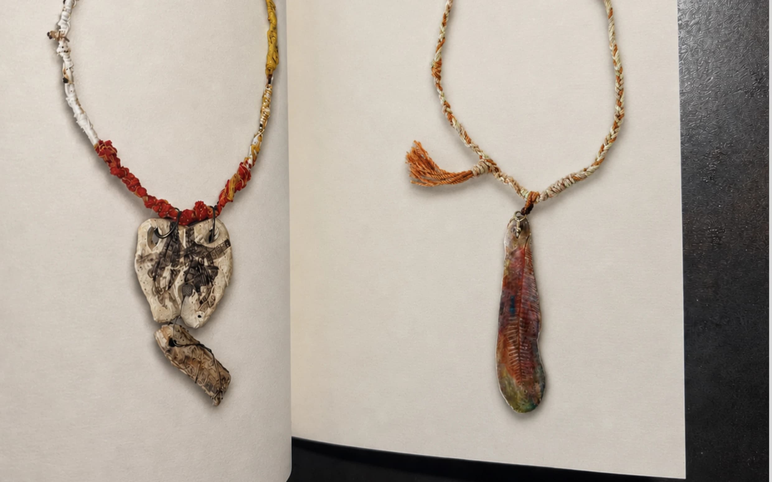 Two necklaces with ceramic pendants displayed across an open portfolio.