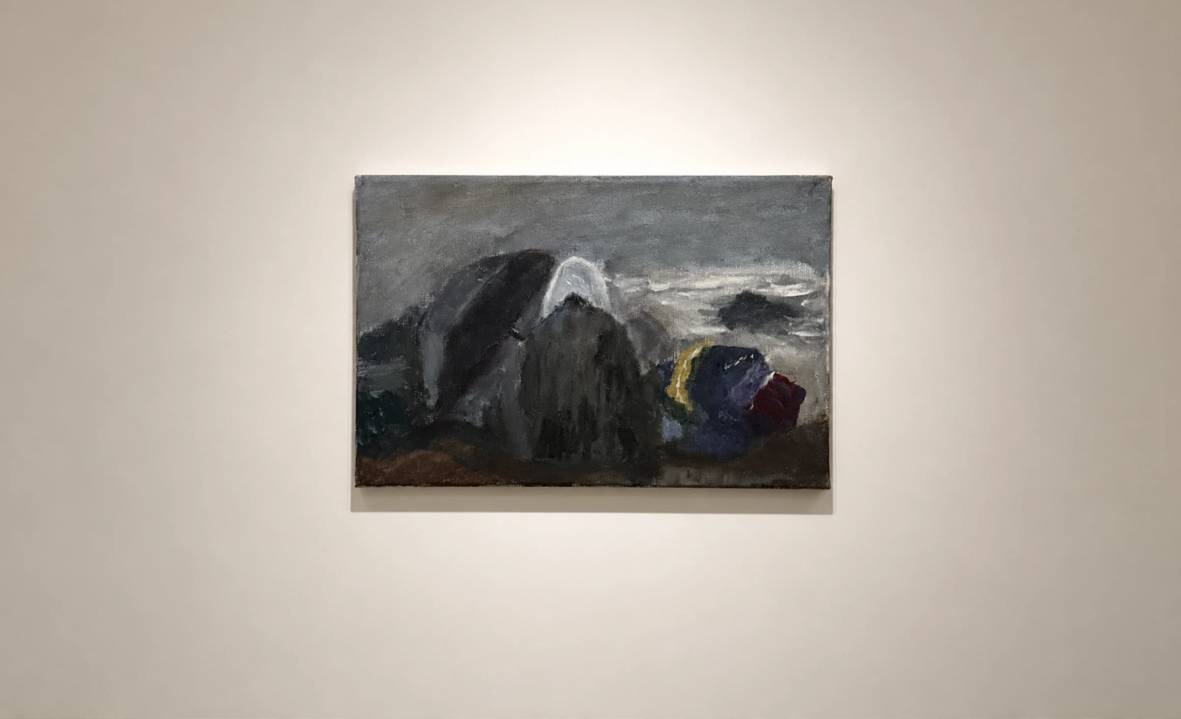 A dark mountain-like form with pale and colored shapes, on a gallery wall.