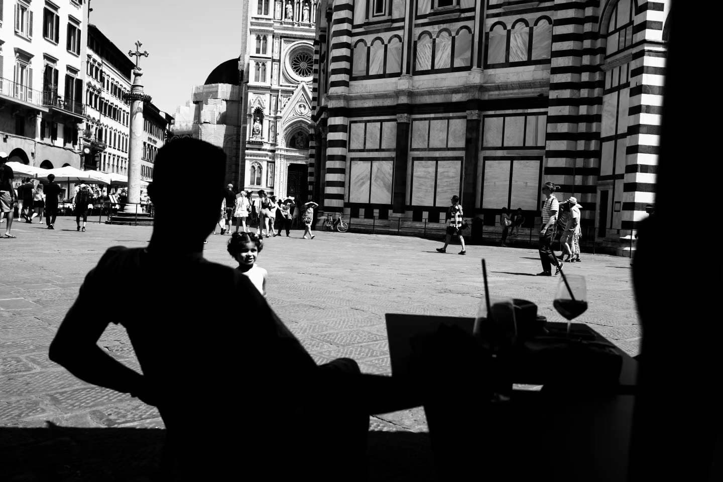 A silhouetted figure beside a café window facing an ornate building.